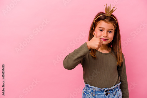 Little princess girl with crown isolated on pink background smiling and raising thumb up