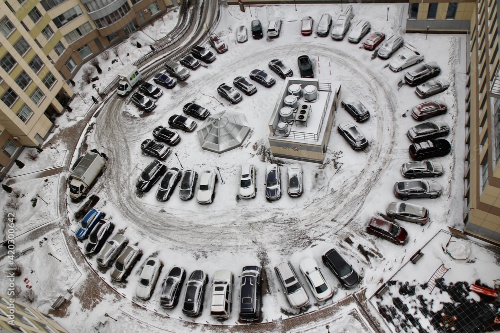 A circular parking in the courtyard of a residential building with snow-covered cars on a gloomy winter morning.