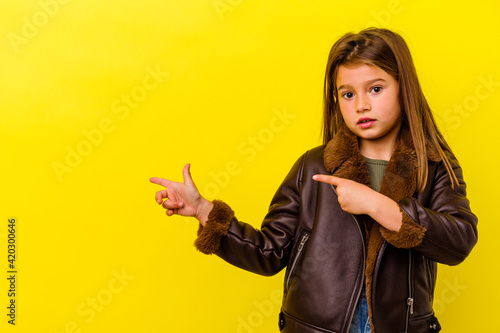 Little caucasian girl isolated on yellow background shocked pointing with index fingers to a copy space.