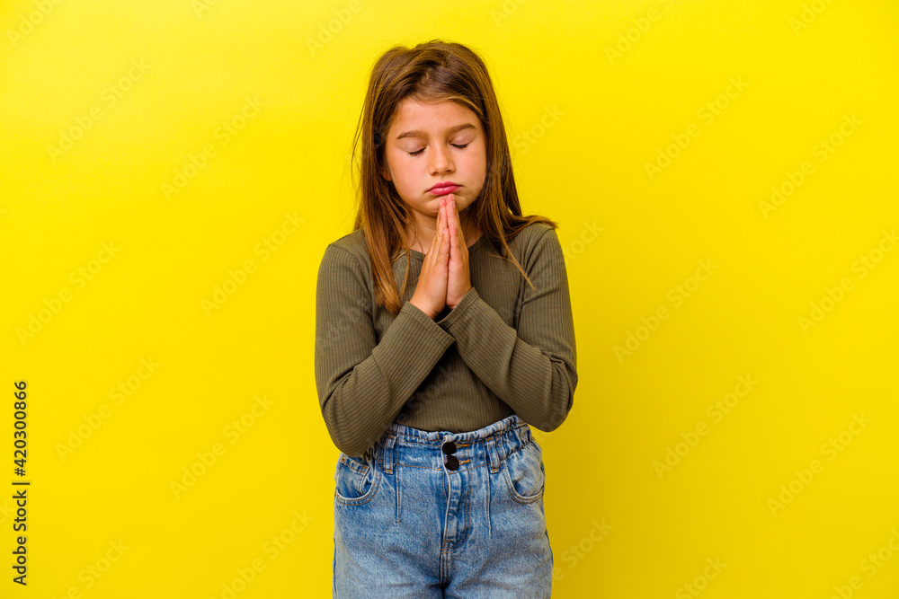 Little caucasian girl isolated on yellow background praying, showing devotion, religious person looking for divine inspiration. Little caucasian girl isolated on yellow background praying, showing devotion, religious person looking for divine inspiration.