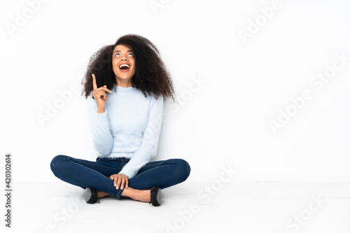 Young african american woman sitting on the floor pointing up and surprised