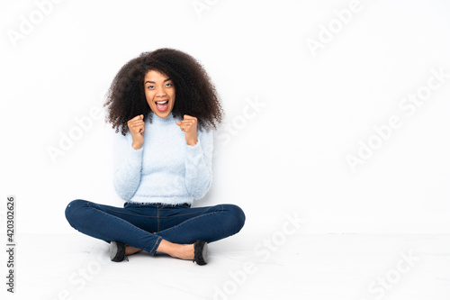 Young african american woman sitting on the floor celebrating a victory in winner position