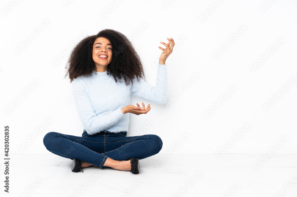 Young african american woman sitting on the floor extending hands to the side for inviting to come Young african american woman sitting on the floor extending hands to the side for inviting to come