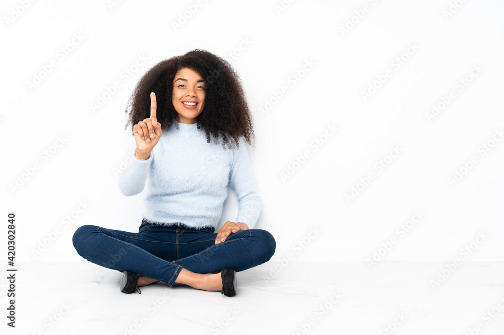 Young african american woman sitting on the floor showing and lifting a finger Young african american woman sitting on the floor showing and lifting a finger