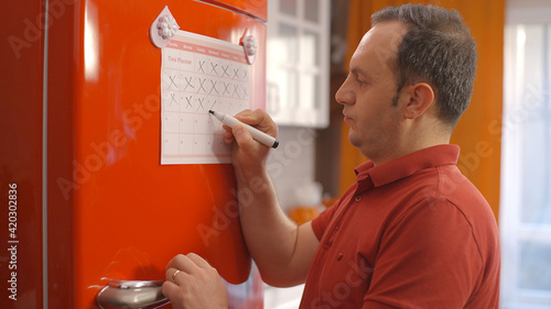 The man who follows the flow of time on his diet program in the refrigerator. The young man counts his schedule and marks it with a pencil.