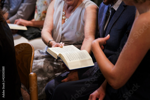 In der Kirche sitzen viele Leute, eine Frau übergibt einem Mann eine Bibel. Alle sind schick angezogen. Es könnte eine Hochzeit, Kommunion oder Konfirmation sein.