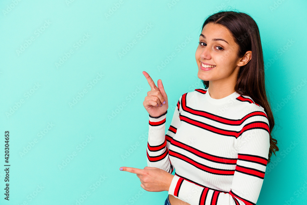 Young Indian woman isolated on blue background excited pointing with forefingers away. Young Indian woman isolated on blue background excited pointing with forefingers away.