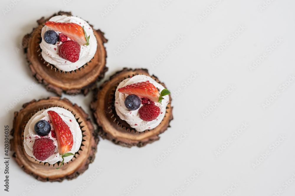 red cream cupcakes with strawberries and blueberries on natural wood coasters red cream cupcakes with strawberries and blueberries on natural wood coasters