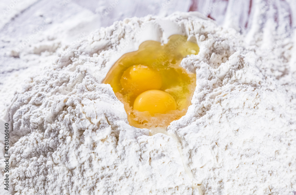 Baking scenery with a heap of wheat white flour for kneading dough for pasta or pizza with a raw egg on top. Close up. Homemade baking concept. Baking scenery with a heap of wheat white flour for kneading dough for pasta or pizza with a raw egg on top. Close up. Homemade baking concept.