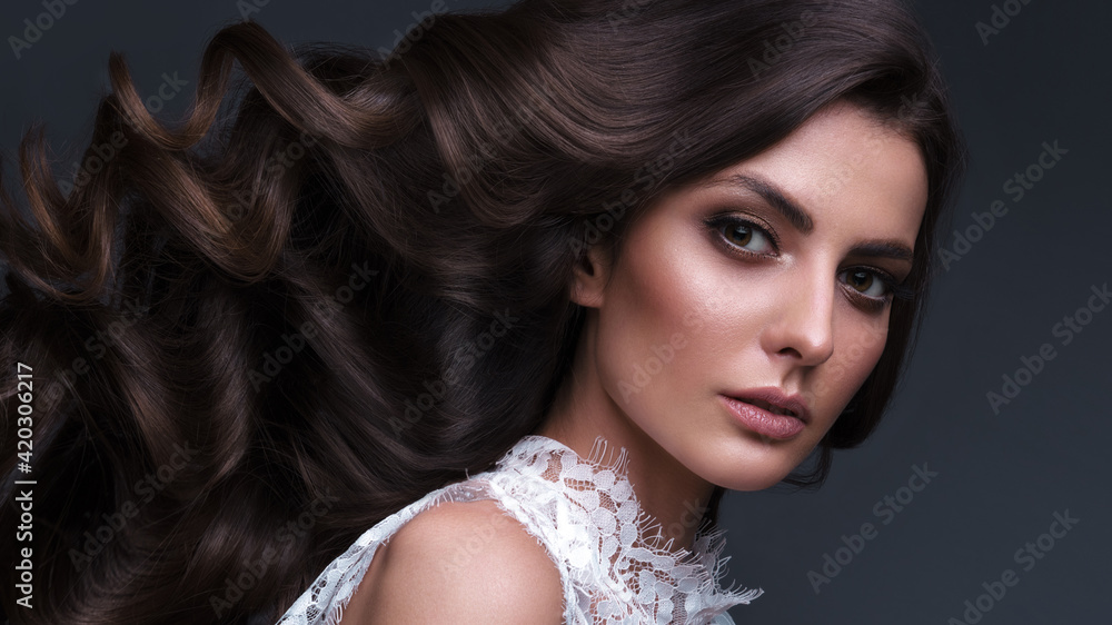 Fototapeta premium Beautiful brown-haired girl with a perfectly curls hair, and classic make-up. Beauty face and hair.