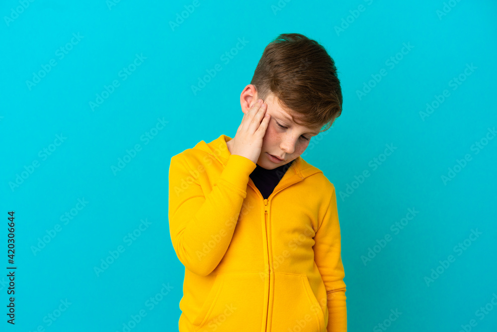 Little redhead boy isolated on blue background with headache Little redhead boy isolated on blue background with headache