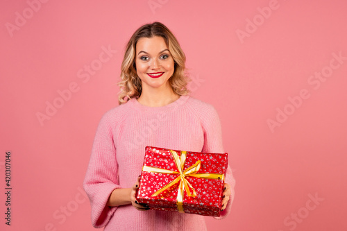 Winter holiday, a young woman in a pink sweater on a pink background © Alexander