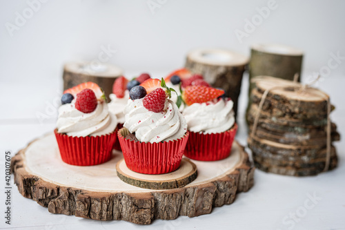 red cream cupcakes with strawberries and blueberries on natural wood coasters