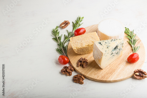 Blue cheese and various types of cheese with rosemary and tomatoes on wooden board on a white background . Side view, copy space.