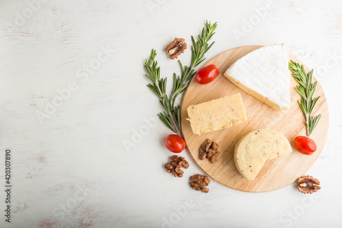 Cheddar and various types of cheese with rosemary and tomatoes on wooden board on a white background . Top view, copy space.