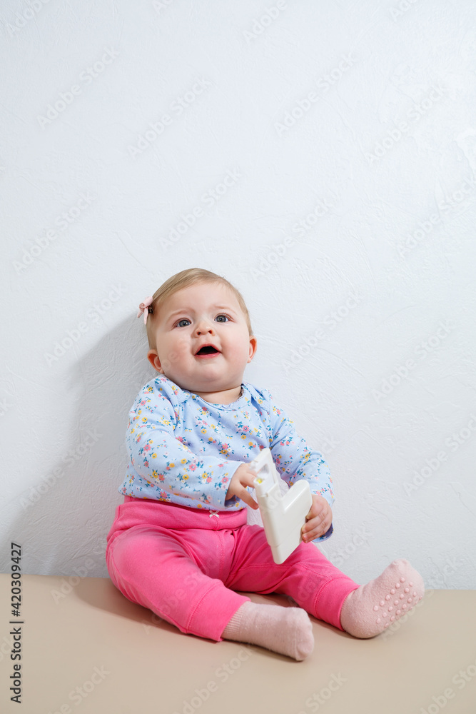 A little girl, eight months old, is sitting on the couch holding an ear piercing device. Beauty for young children A little girl, eight months old, is sitting on the couch holding an ear piercing device. Beauty for young children