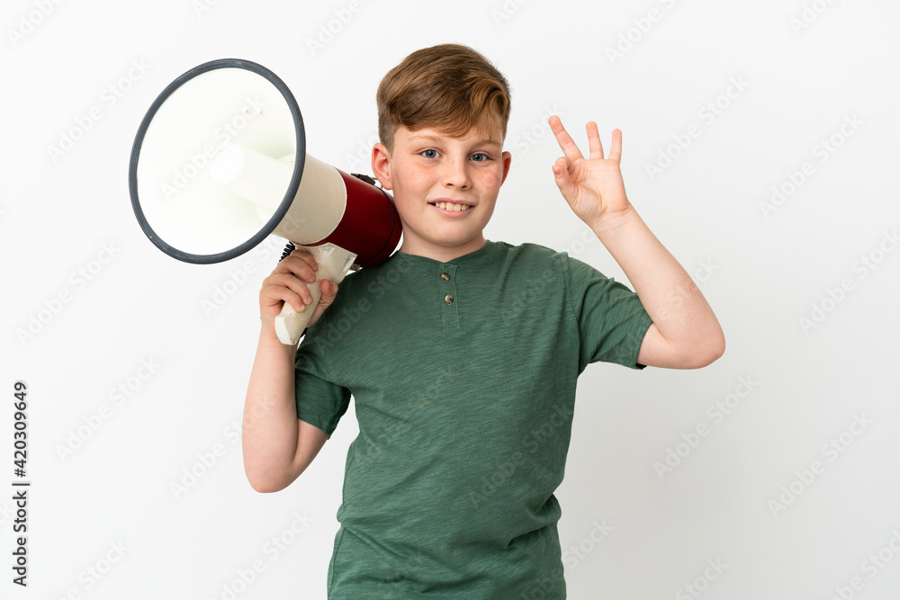 Little redhead boy isolated on white background holding a megaphone and showing ok sign with fingers