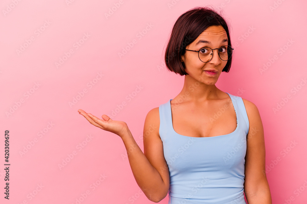 Young mixed race woman isolated on pink background showing a copy space on a palm and holding another hand on waist. Young mixed race woman isolated on pink background showing a copy space on a palm and holding another hand on waist.