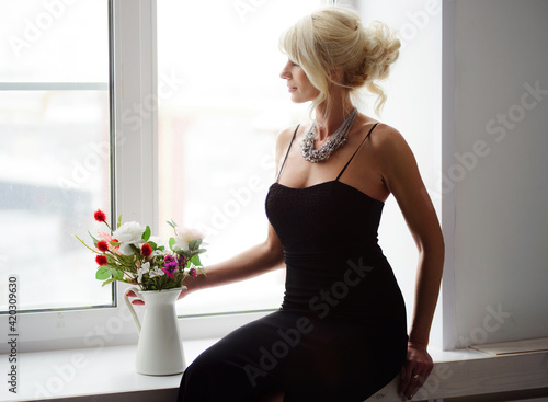 beautiful adult blonde woman with a bouquet of flowers on a spring morning near the window