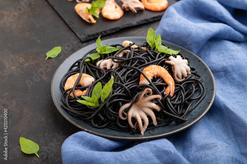 Black cuttlefish ink pasta with shrimps or prawns and small octopuses on gray wooden background. Side view.