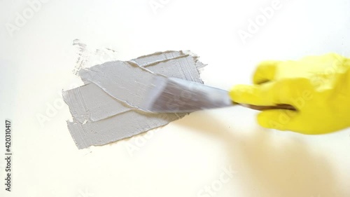 A hand in a rubber yellow glove holds a spatula and putty the board photo