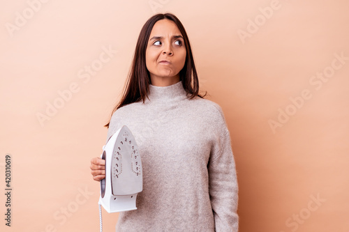 Young mixed race woman holding an iron isolated confused, feels doubtful and unsure.