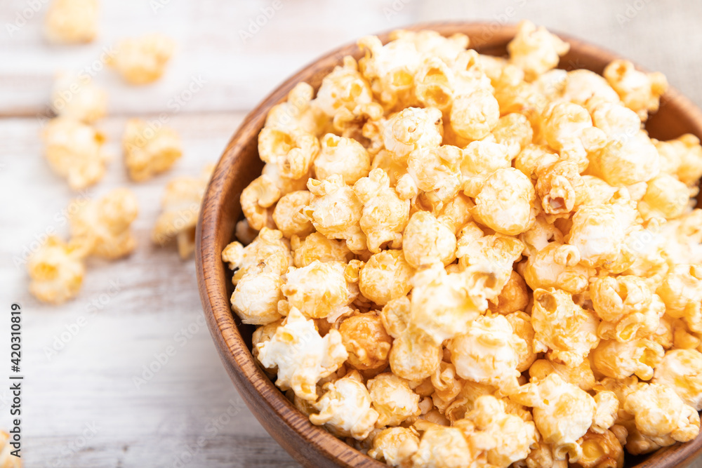 Popcorn with caramel in wooden bowl and a cup of coffee on a white wooden background. Side view, selective focus. Popcorn with caramel in wooden bowl and a cup of coffee on a white wooden background. Side view, selective focus.