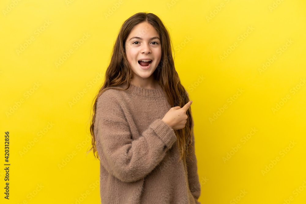 Little caucasian girl isolated on yellow background surprised and pointing side Little caucasian girl isolated on yellow background surprised and pointing side