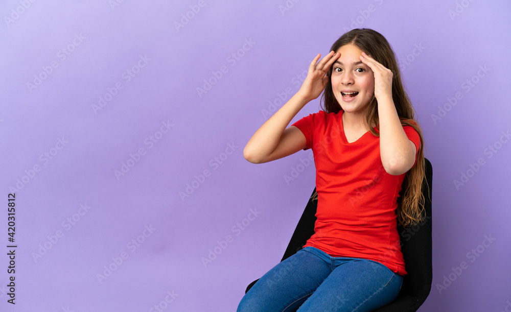 Little caucasian girl sitting on a chair isolated on purple background with surprise expression