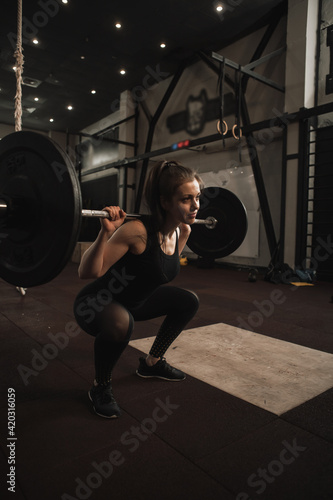 Vertical shot of a sportswoman doing barbell squats at the gym