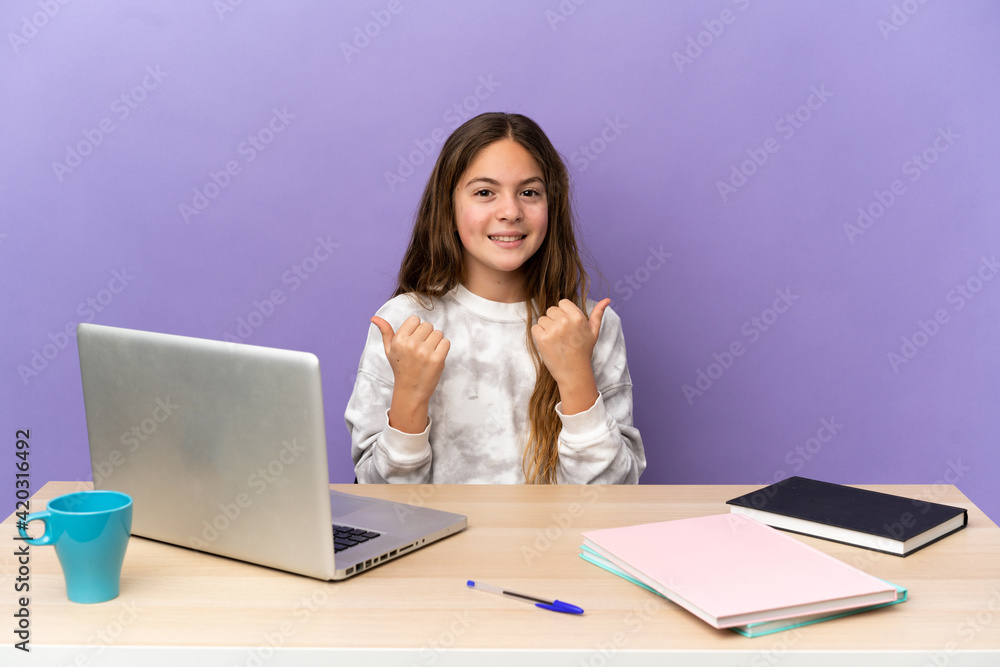 Little student girl in a workplace with a laptop isolated on purple background with thumbs up gesture and smiling Little student girl in a workplace with a laptop isolated on purple background with thumbs up gesture and smiling