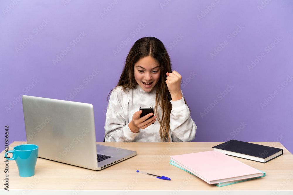 Little student girl in a workplace with a laptop isolated on purple background surprised and sending a message Little student girl in a workplace with a laptop isolated on purple background surprised and sending a message
