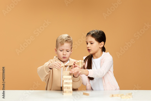 children plays with wooden constructor on desk.