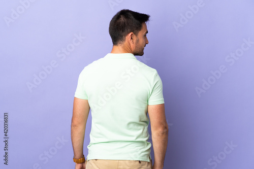 Young handsome man isolated on purple background in back position and looking side