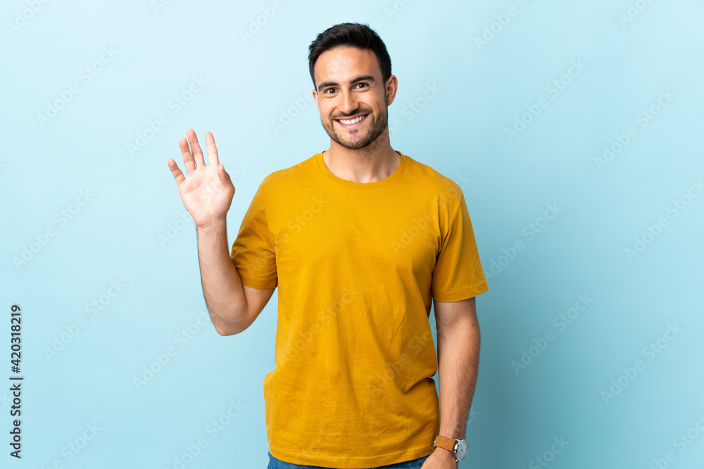 Young handsome man over isolated background saluting with hand with happy expression Young handsome man over isolated background saluting with hand with happy expression