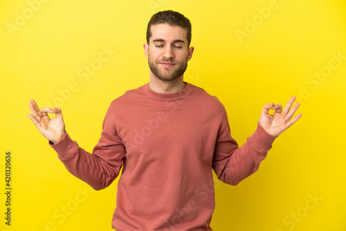 Handsome blonde man over isolated yellow background in zen pose