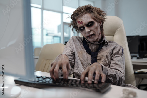 Tableau sur toile Spooky businessman with zombie body painting looking at computer screen and typi