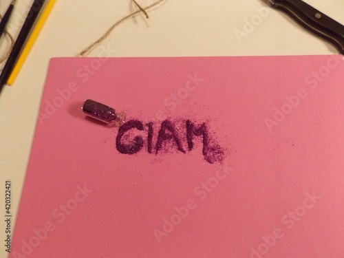 Glam misspelled in pink glitter on pink paper on crafts table