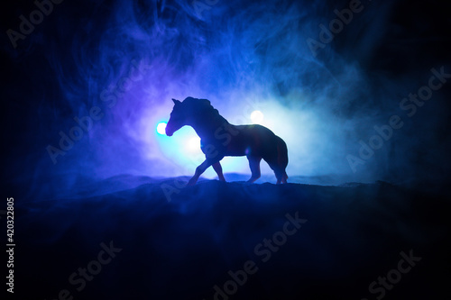 Beautiful horse running in desert at night. Silhouette of a horse miniature standing at foggy night. Creative table decoration with colorful backlight with fog. Selective focus