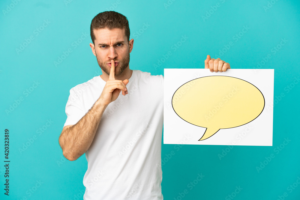 Handsome blonde man over isolated blue background holding a placard with speech bubble icon doing silence gesture