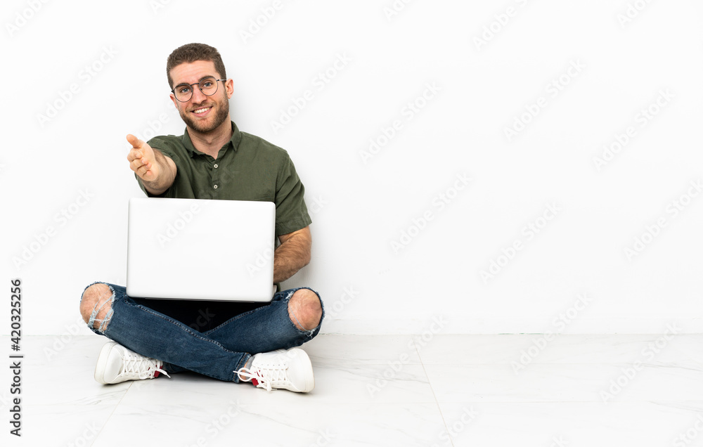 Young man sitting on the floor shaking hands for closing a good deal Young man sitting on the floor shaking hands for closing a good deal