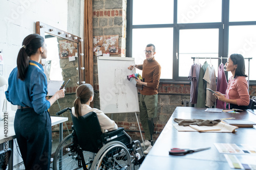 Young disable male designer with textile samples standing by whiteboard while explaining his view © pressmaster