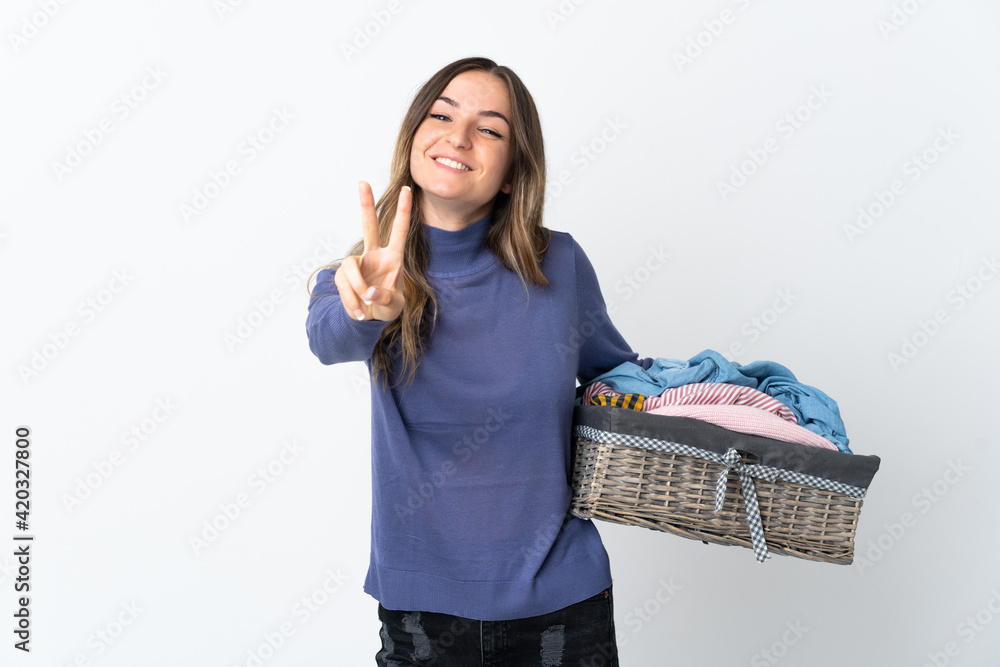 Young woman holding a clothes basket isolated on background smiling and showing victory sign Young woman holding a clothes basket isolated on background smiling and showing victory sign