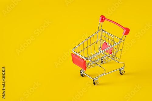Empty red shopping cart on yellow background, mini metal cart isolated on yellow background, copy space for text