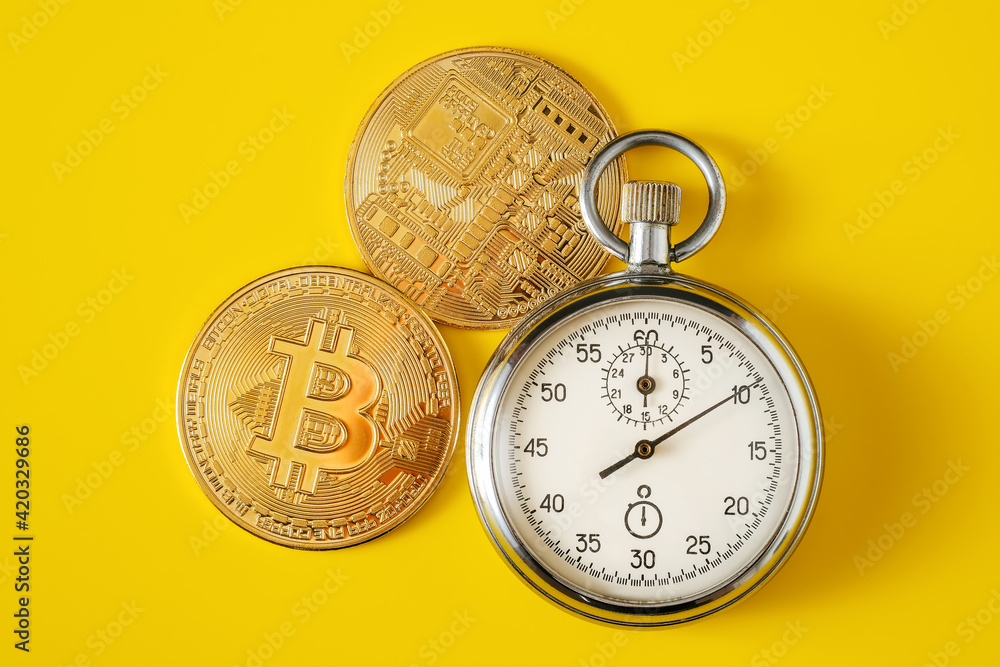Golden bitcoin coin and stopwatch on yellow monochrome background. Top view, time is money concept Golden bitcoin coin and stopwatch on yellow monochrome background. Top view, time is money concept