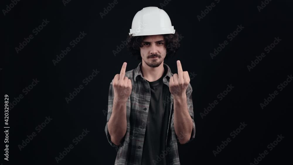 Irritated engineer wearing a special helmet on his head, dressed in a plaid shirt, on a black background, in the studio, raising both middle fingers up in disagreement. Irritated engineer wearing a special helmet on his head, dressed in a plaid shirt, on a black background, in the studio, raising both middle fingers up in disagreement.