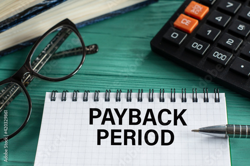Slika na platnu PAYBACK PERIOD - words in a notepad on a wooden green background with a calculat