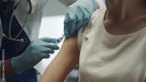 The patient receives a vaccination against the okved - 19 virus strain in her arm. The doctor lubricates the hand with alcohol to give the injection. photo