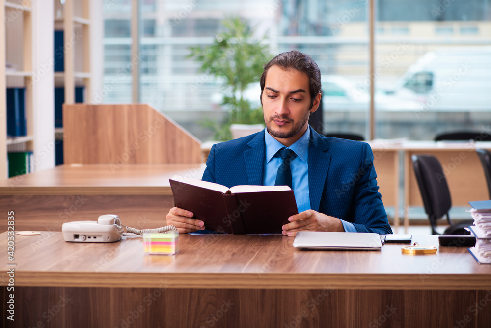 Young male employee reading book in the office