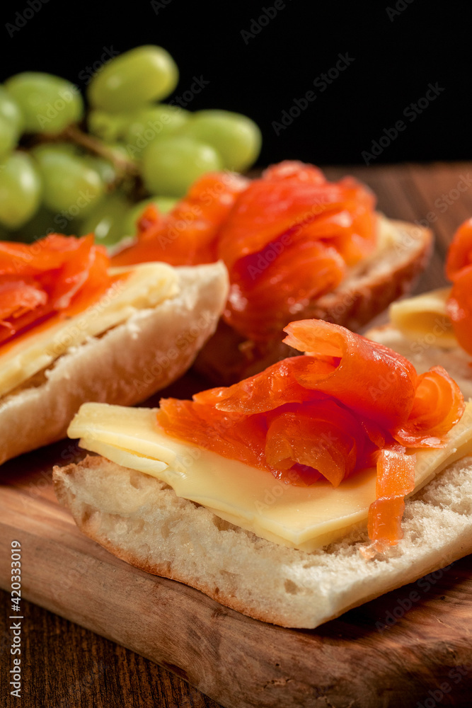 Smoked salmon sandwich with cheese and green grapes on a wooden board. Close up, Selective focus. Black background. Smoked salmon sandwich with cheese and green grapes on a wooden board. Close up, Selective focus. Black background.